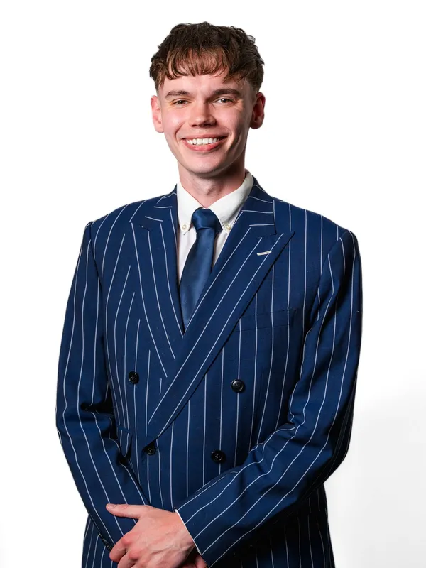 Ethan Mercer standing, smiling, in a navy pinstripe suit and blue tie